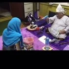 Una persona con un gorro de papel aluminio y vestida de blanco, sentada en un sofá, apunta a otra persona con un objeto mientras esta se aga